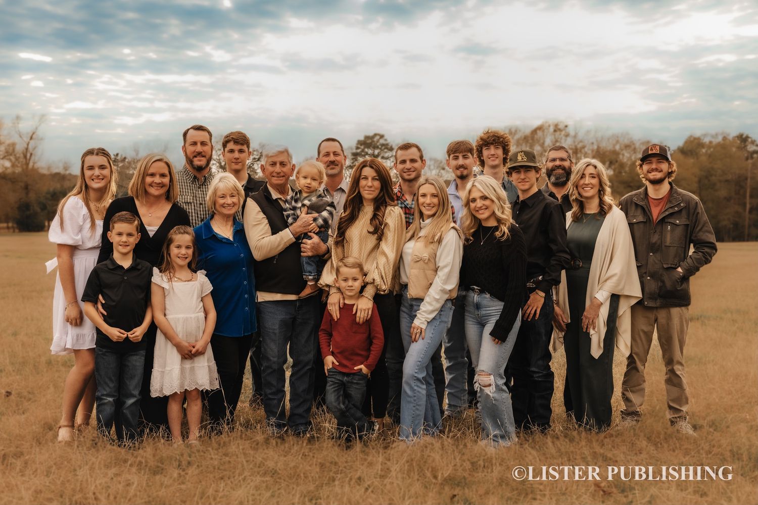 Large group posed outdoors against rustic autumn backdrop.