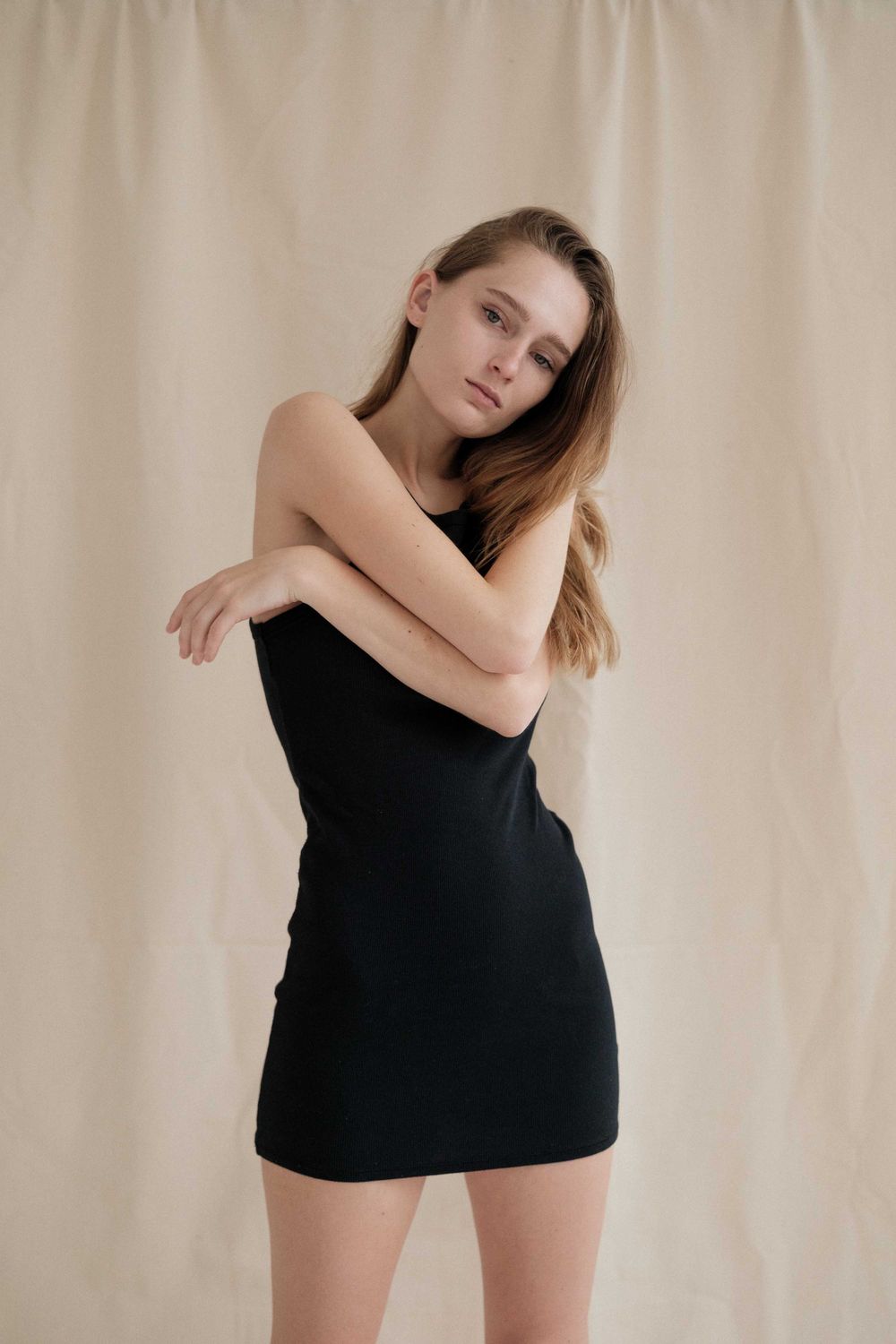 Four artistic black and white portrait photographs against beige backdrop showing figure in minimal black clothing.