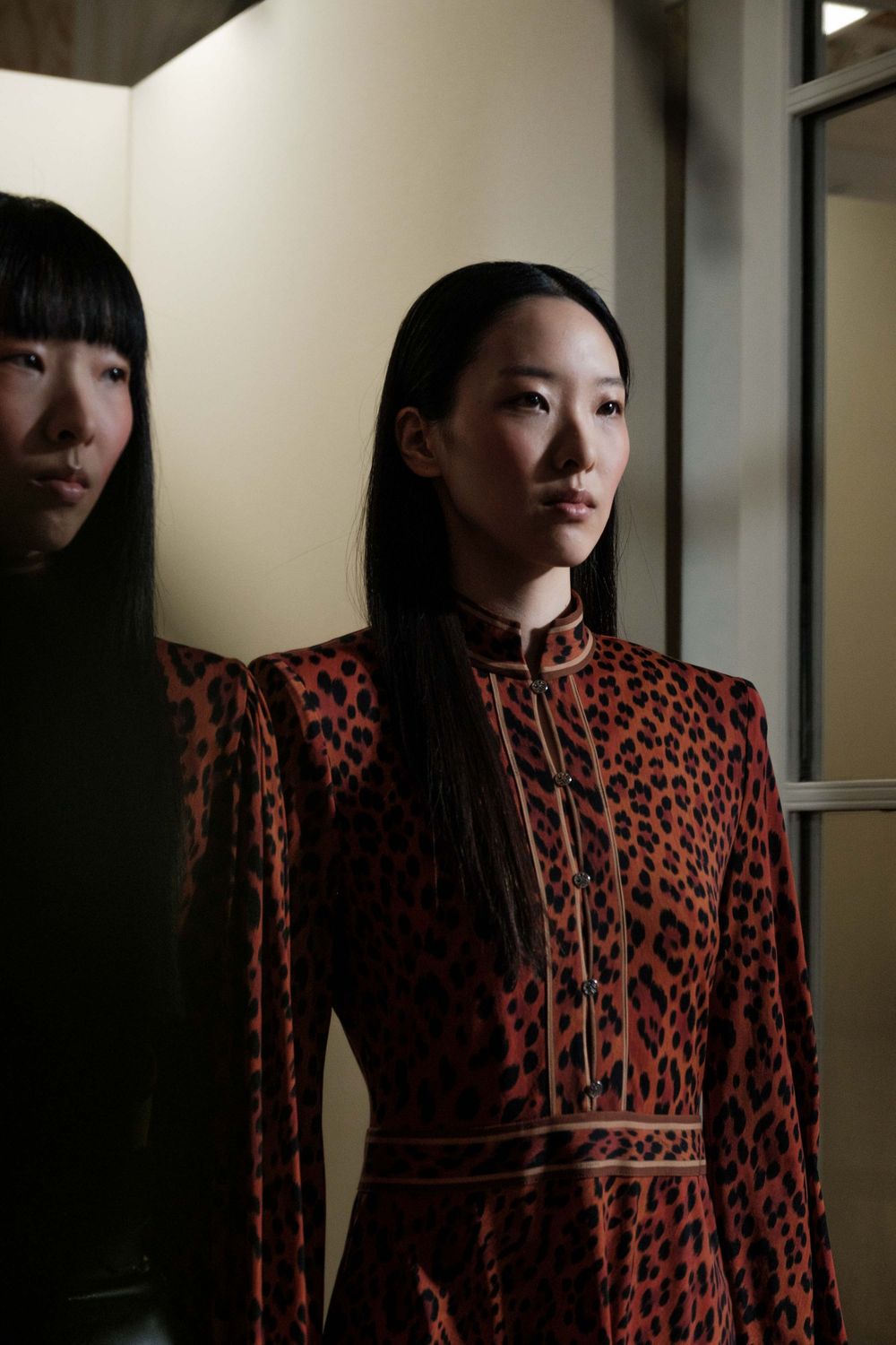 Model wearing a red and black patterned dress with structured shoulders in an elegant indoor setting.