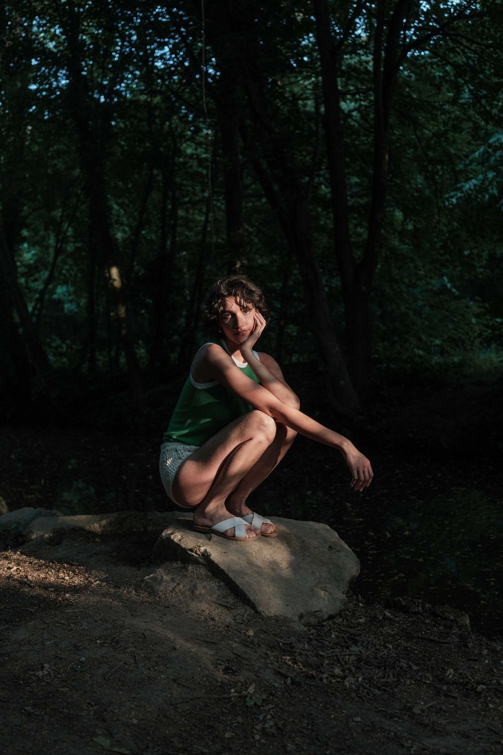 A figure crouches in artistic poses on a large rock in a dark wooded setting.