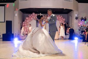 Father and daughter share emotional first dance at quinceañera with pink balloon arch in background.