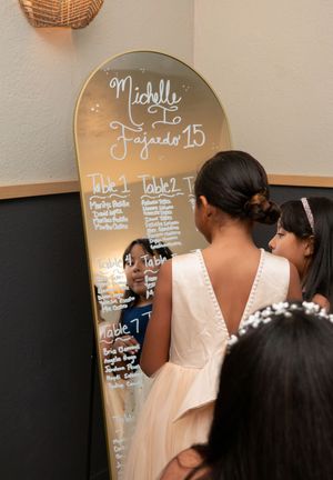 Quinceañera honoree Michelle Fajardo reads seating chart written on decorative gold mirror at her 15th.