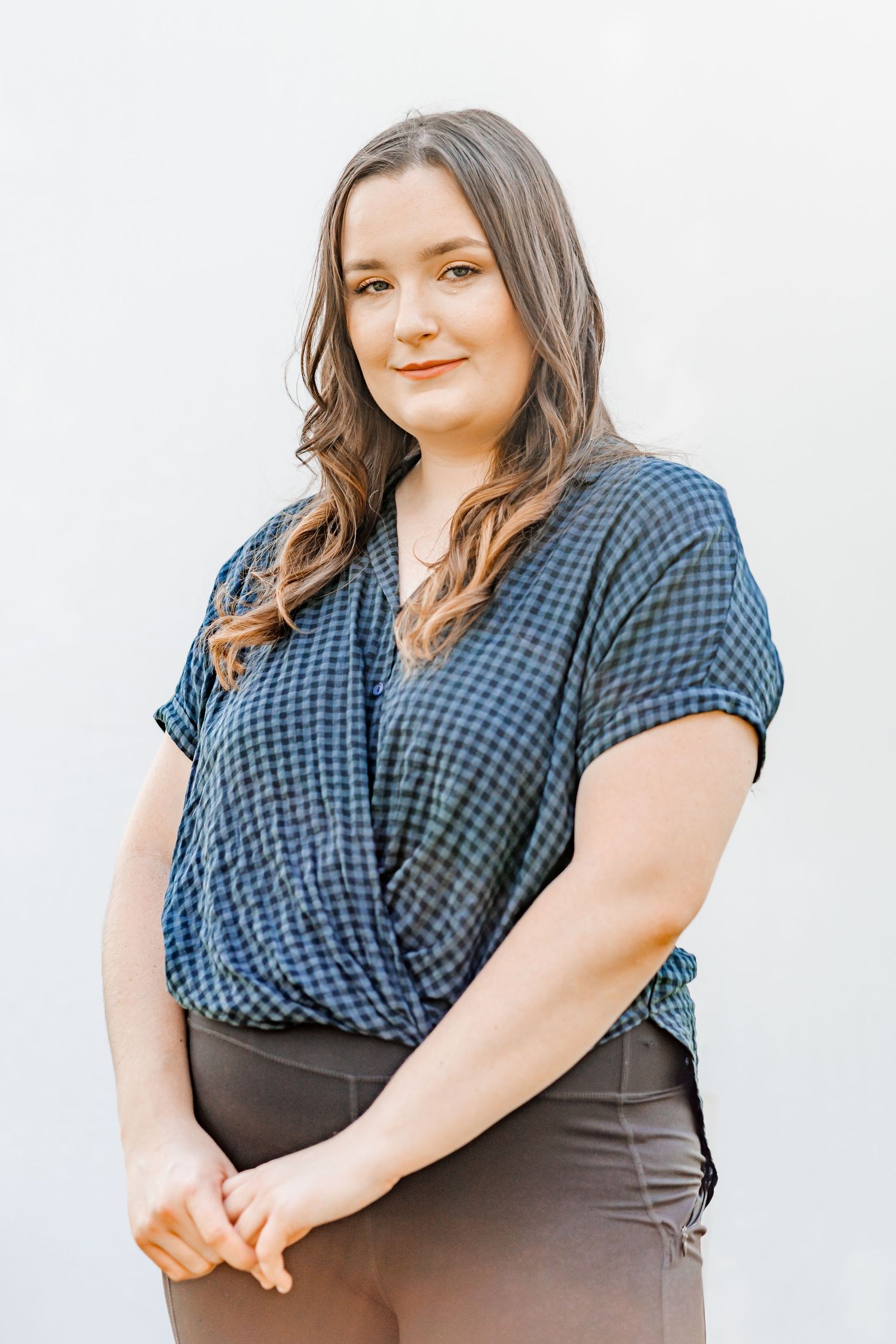 Smiling woman standing in front of a light-colored pop-up backdrop, relaxed and confident in an outdoor portrait session.