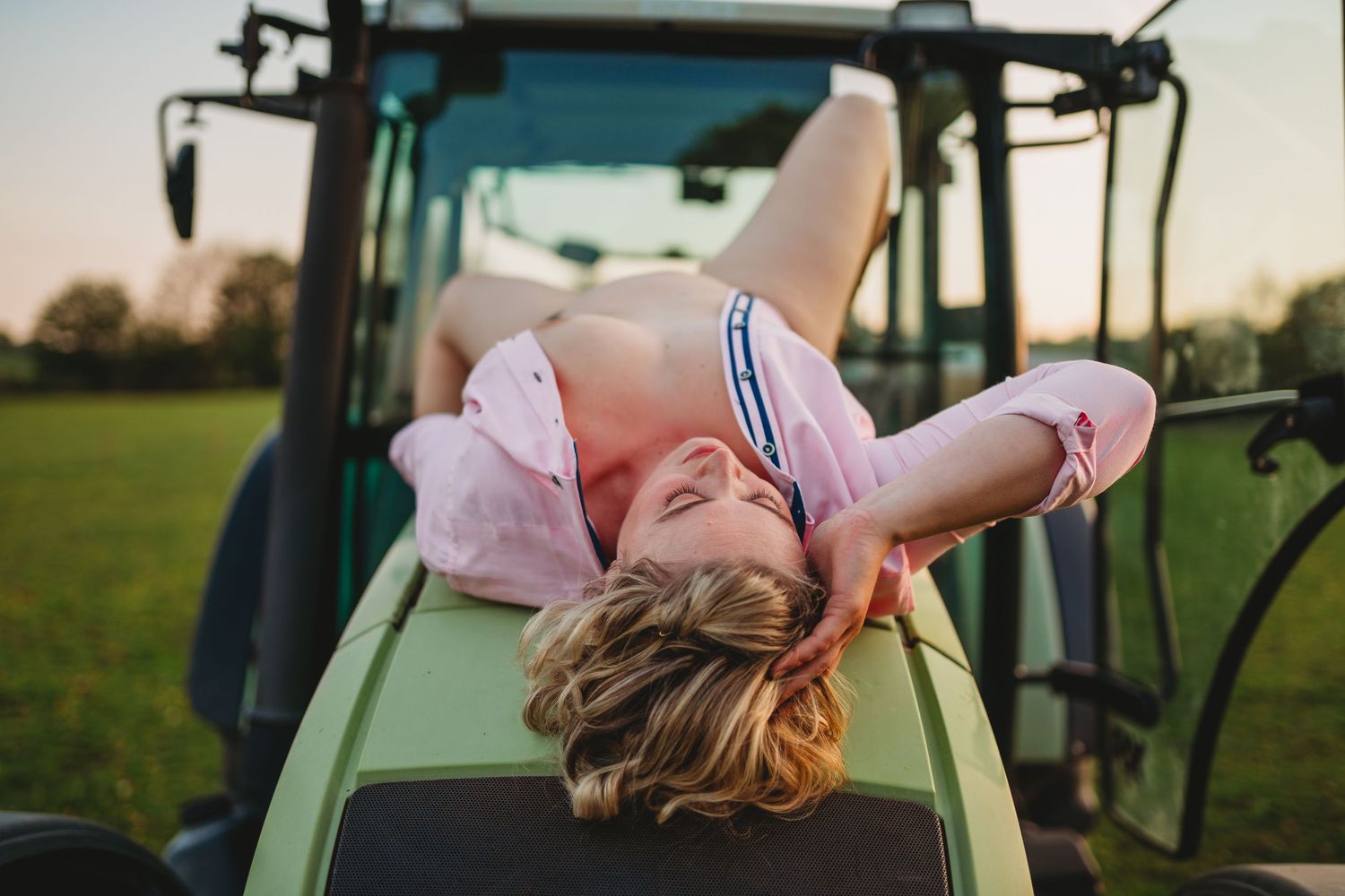 Someone sits on a green tractor in casual attire during golden hour.