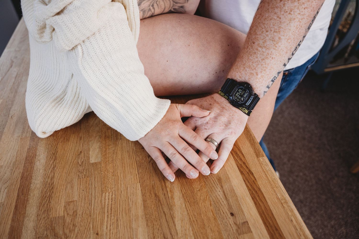 Close-up details of hands resting on a wooden surface in natural light.