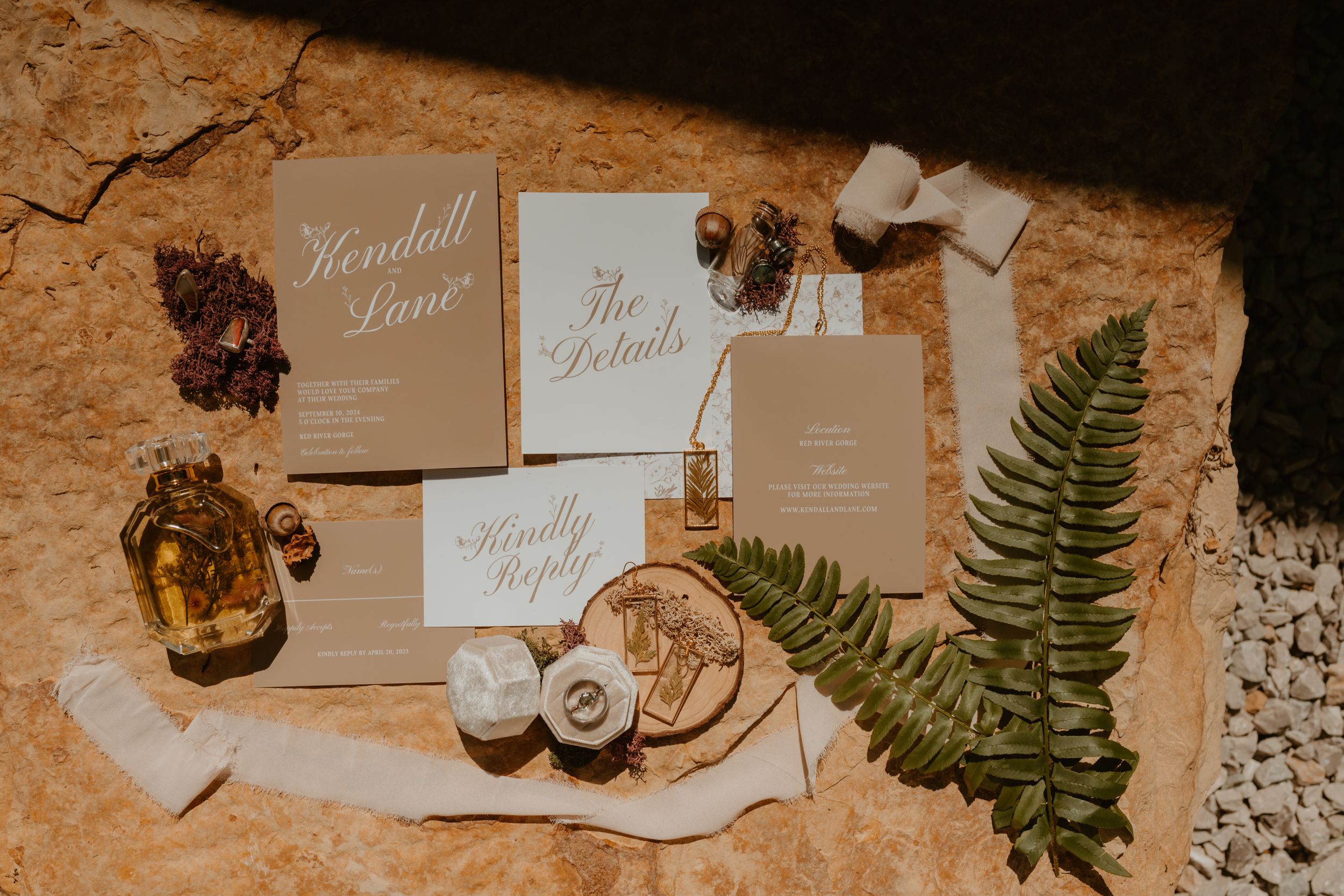 Elegant wedding stationery with calligraphy, set against a rustic surface, decorated with greenery and nature items.