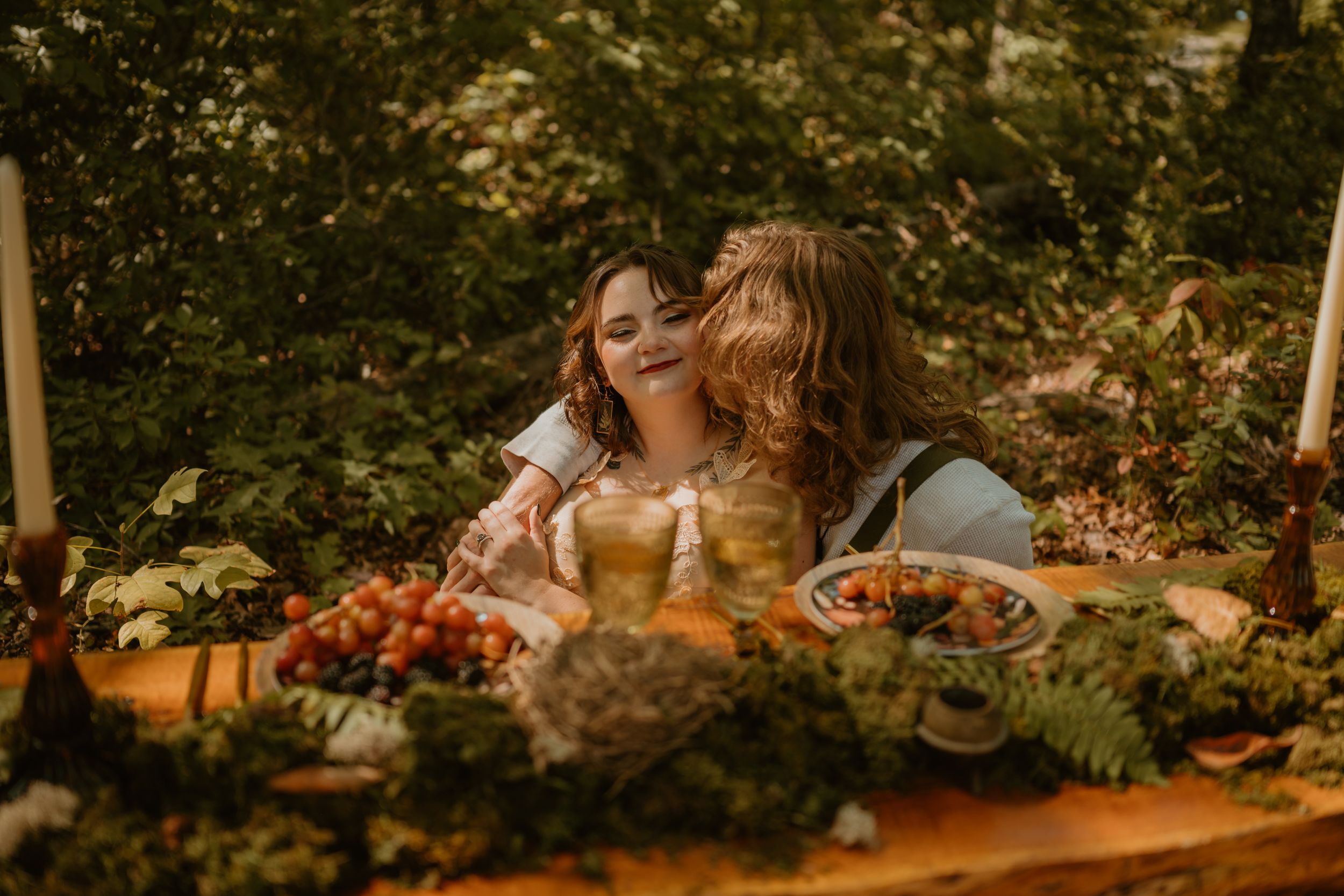 The couple shares an intimate moment at their reception table adorned with food, surrounded by lush greenery.