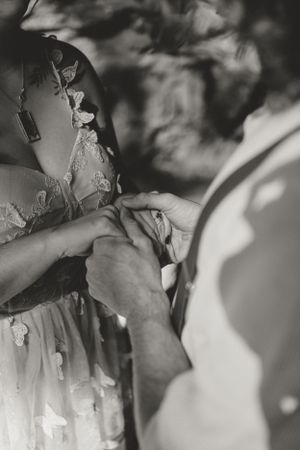 Black and white image of the couple in wedding attire holding hands after exchanging rings..