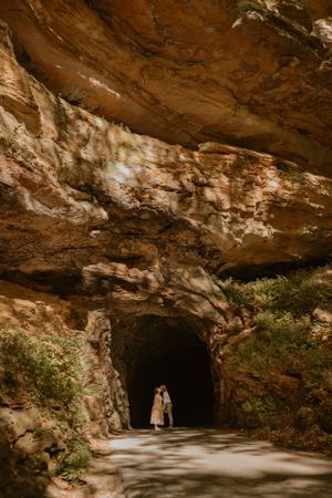 Kendall and Lane share a kiss at their elopement, with greenery around and light shining through above the cave opening.