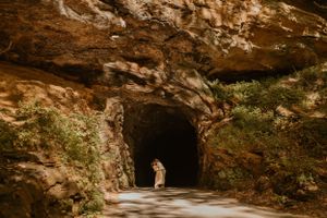 Wide shot of Kendall and Lane's first kiss in front of a rocky cave, sunlight filtering through surrounding foliage.