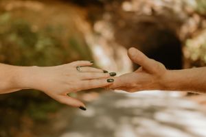 Bride and groom's hands about to touch, the bride with dark green nail polish and a green engagement ring.