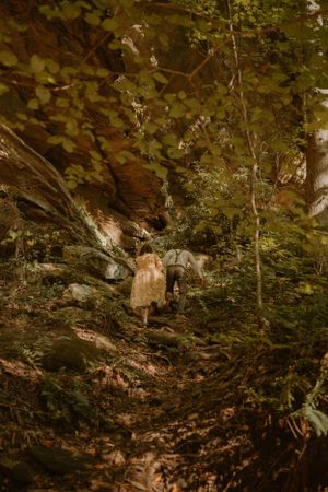 Bride and groom hiking up a wooded trail after their elopement ceremony, sunlight filtering through the trees.