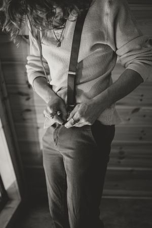 Black and white photo of a groom adjusting suspenders in an A-frame cabin.