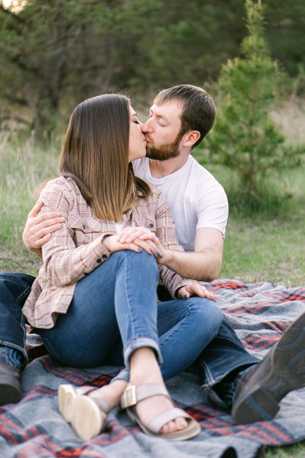 Romantic sunset moment of couple sharing a kiss while sitting on a blanket in a wide-open field, golden light glowing behind them