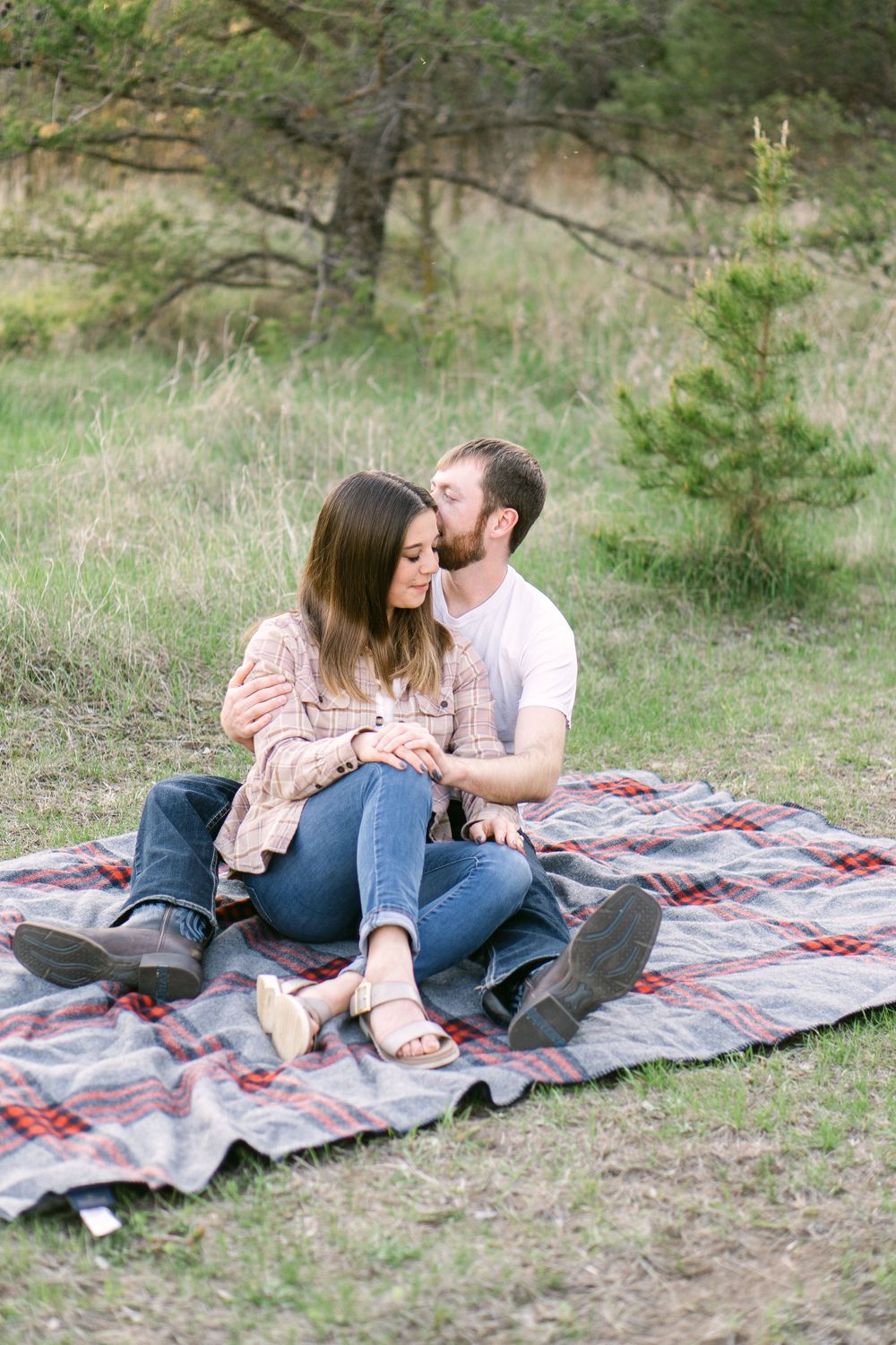 Engaged couple sitting together on a blanket in tall grass during a sunset engagement session near St. Paul, MN