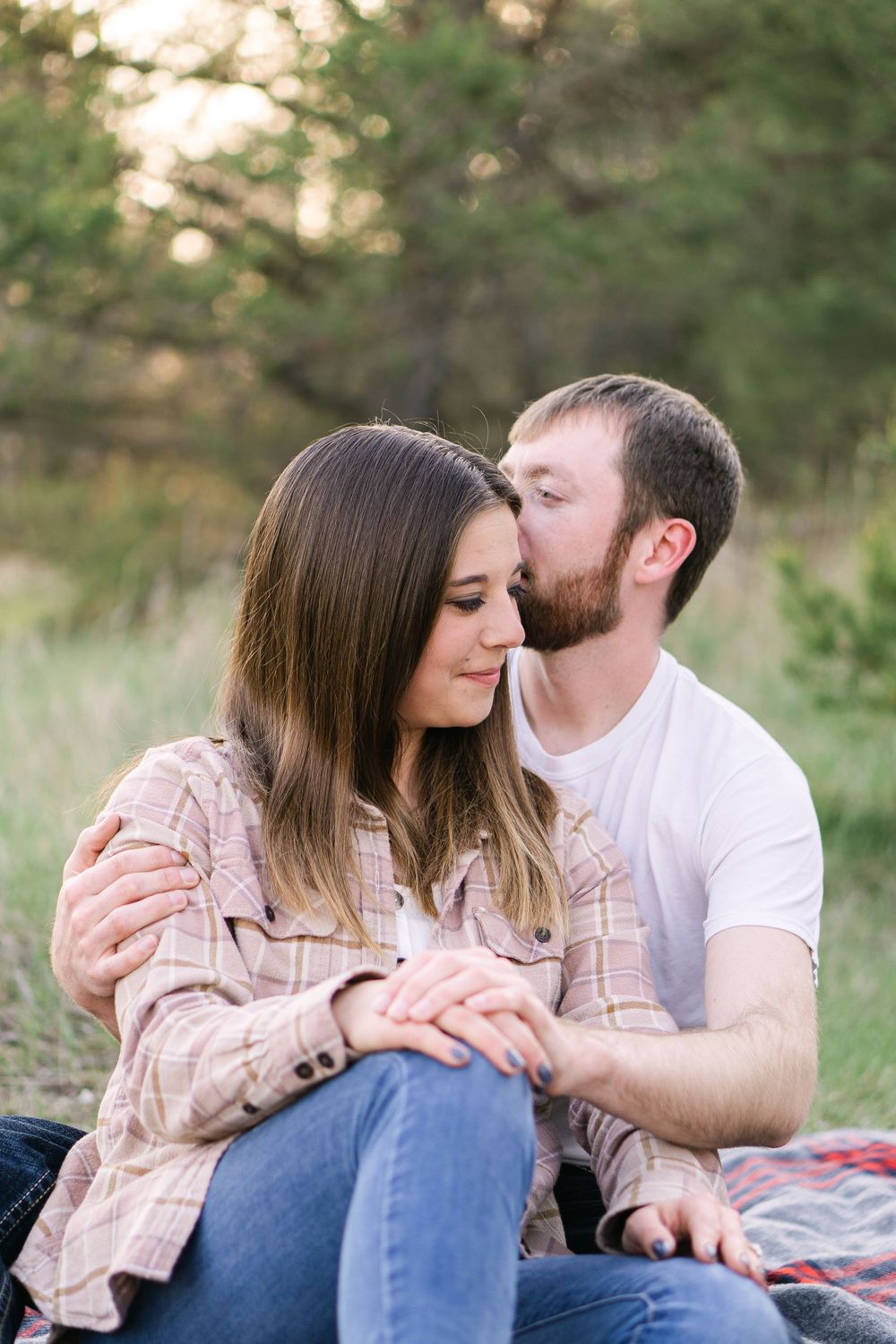 Sweet moment between engaged couple where he kisses her temple as the golden light filters through the trees at golden hour