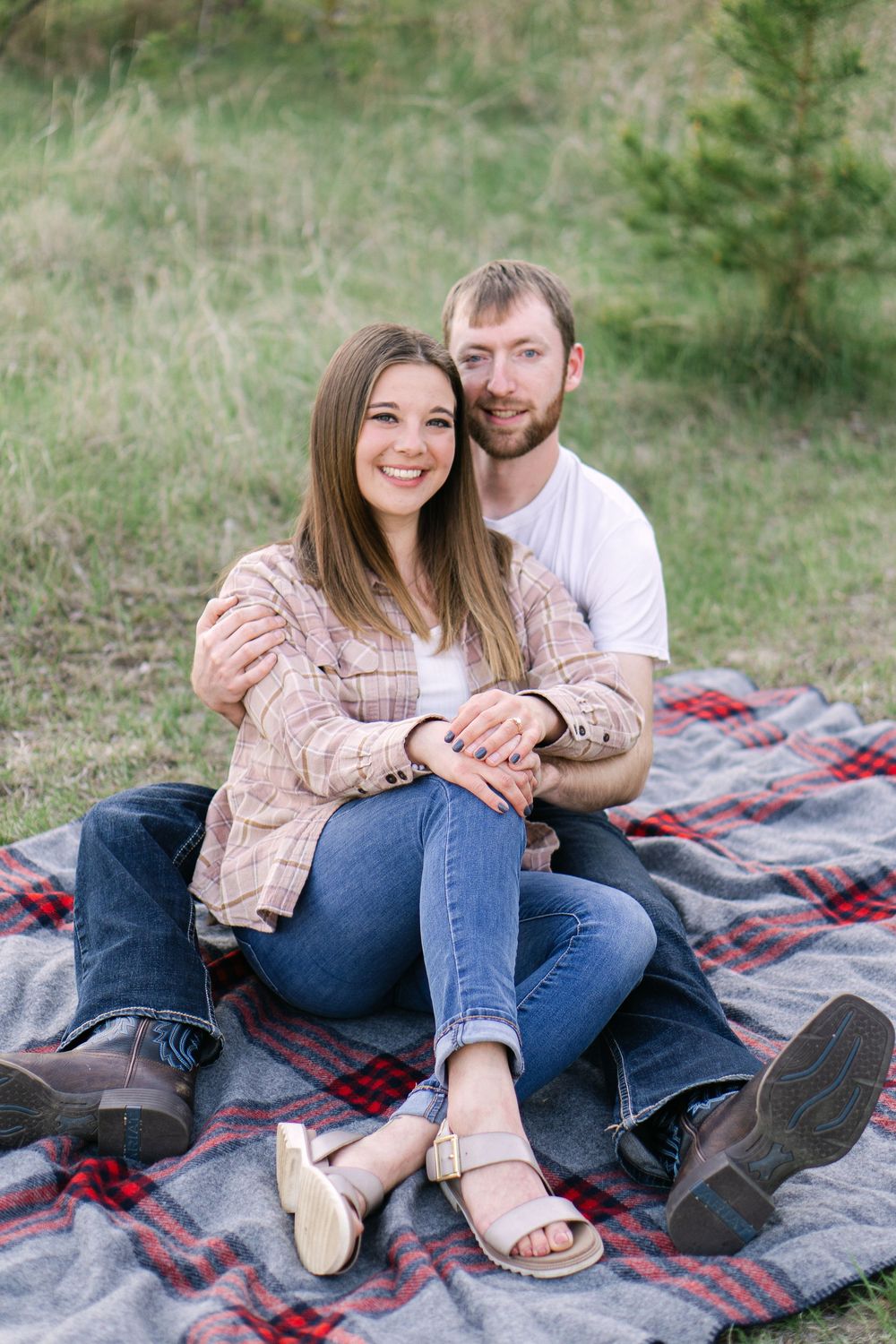 Couple smiling on a blanket  quiet field at sunset during an sweet light and airy engagement session near St. Paul, MN
