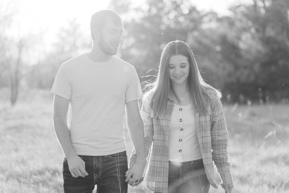 Engaged couple walking through a golden field at sunset during a countryside engagement session in Melrose, Minnesota