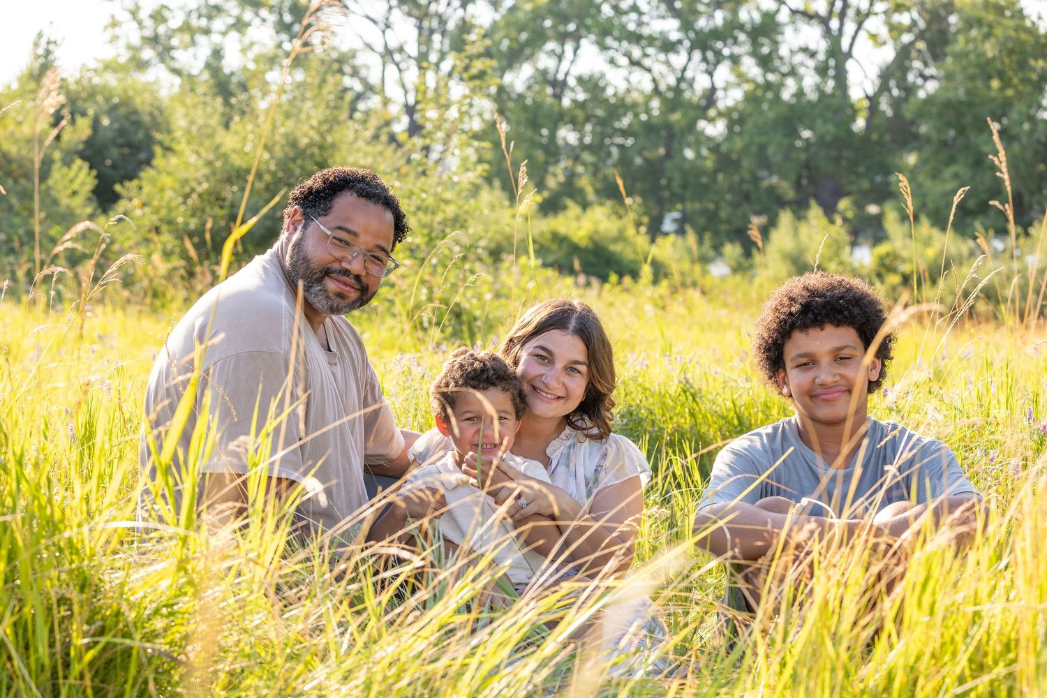 Family relaxing together in tall golden grass during sunset in a meadow.