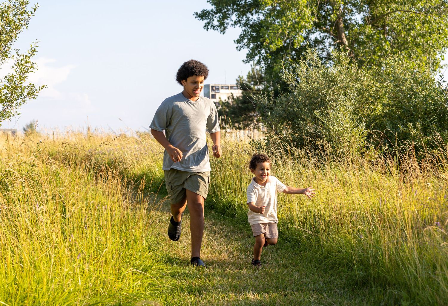 Two people running together on a nature trail through tall summer grass.