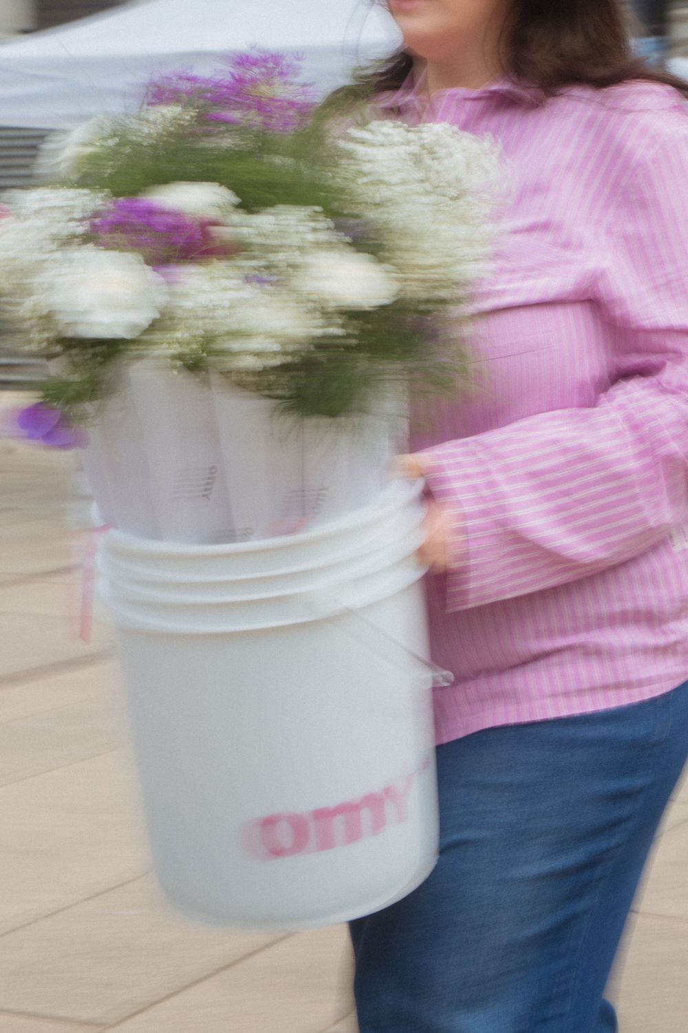 Motion blur of white bucket filled with flowers being carried alongside someone wearing a pink sweater and jeans.