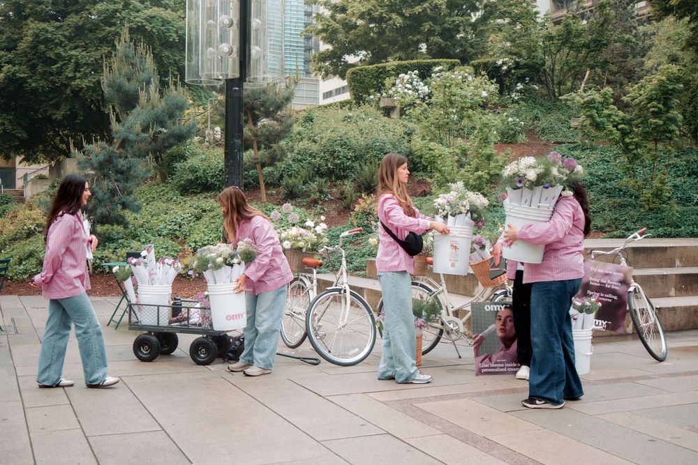 A group in matching pink jackets gathers on steps with bicycles and carts in an outdoor garden setting.