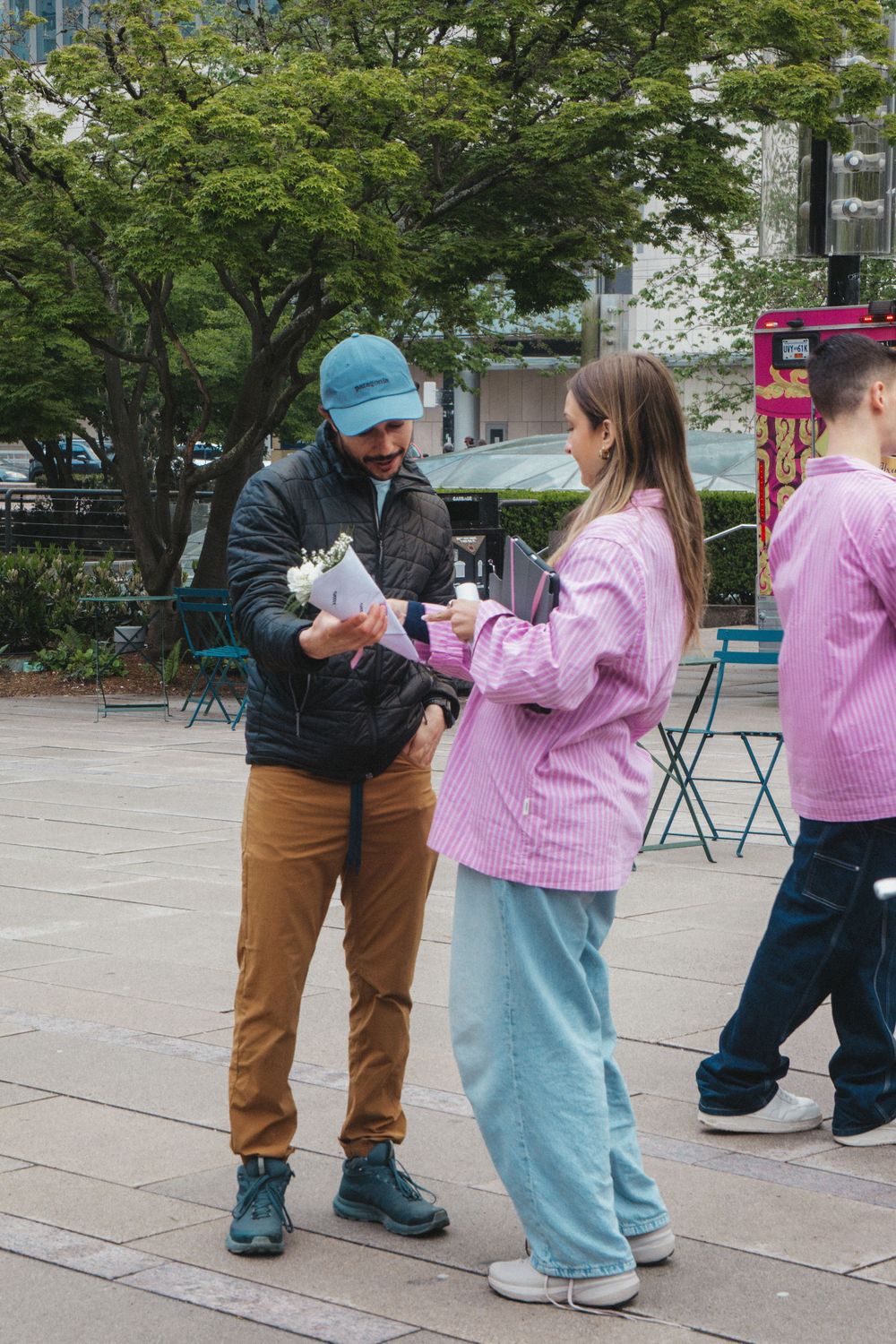 A series of dancers practicing outdoors in pink sweaters and casual attire on a paved courtyard.