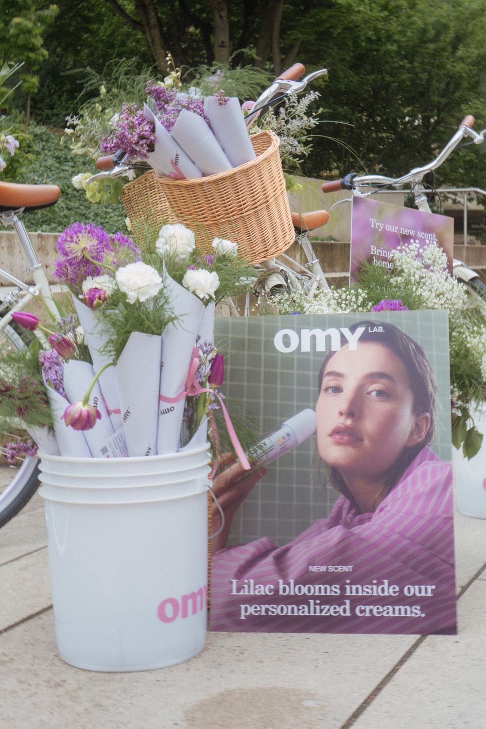 A magazine advertisement display with floral arrangements in white buckets and a wicker basket against a garden backdrop.