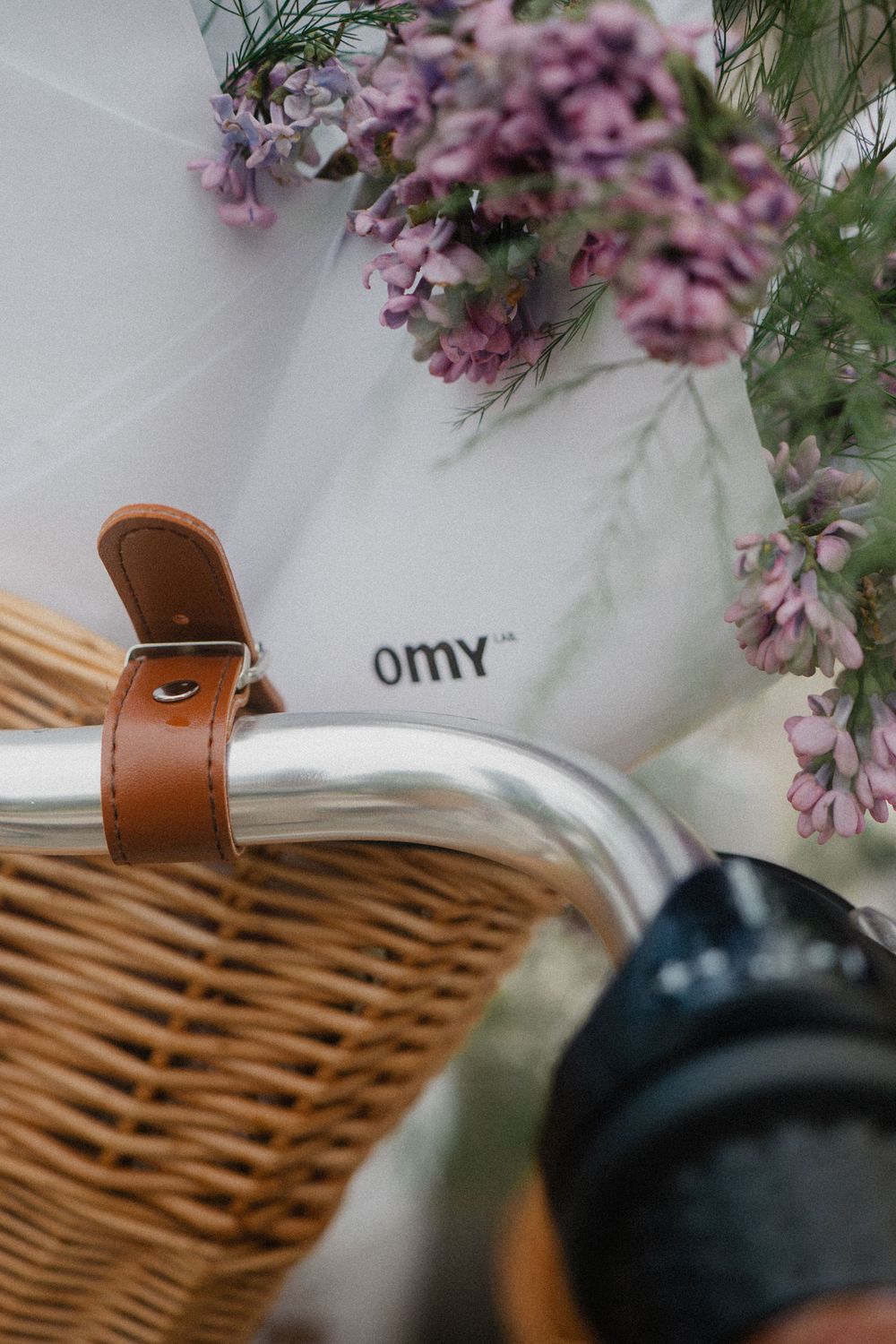Close-up of a wicker basket with leather strap and purple flowers against a white background.