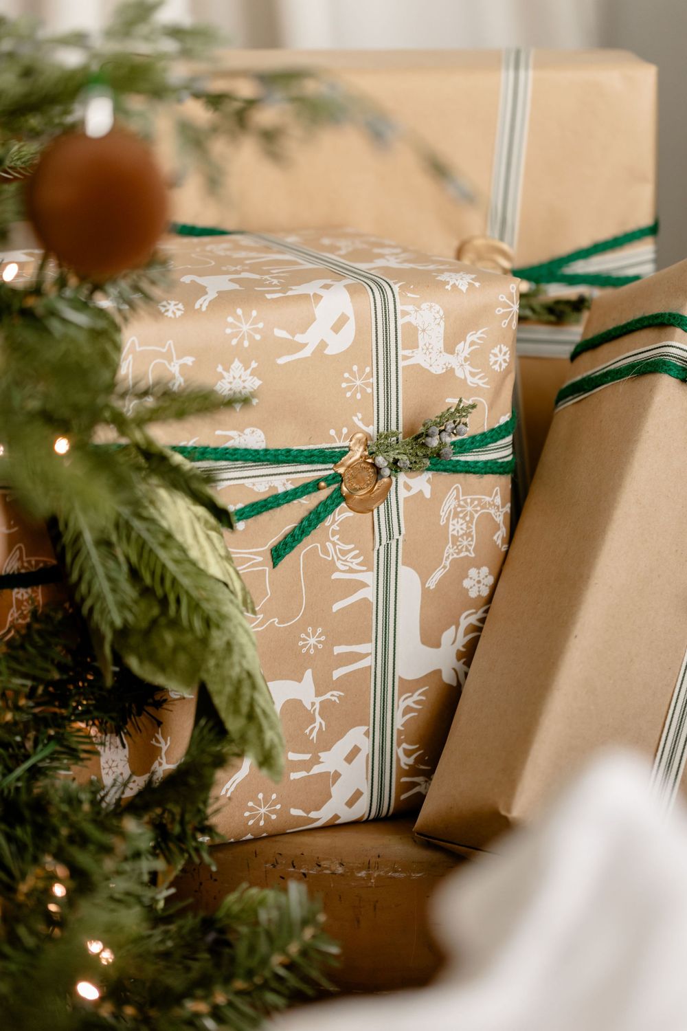Brown kraft paper Christmas presents decorated with white snowflake patterns and green ribbons sit beside evergreen branches.