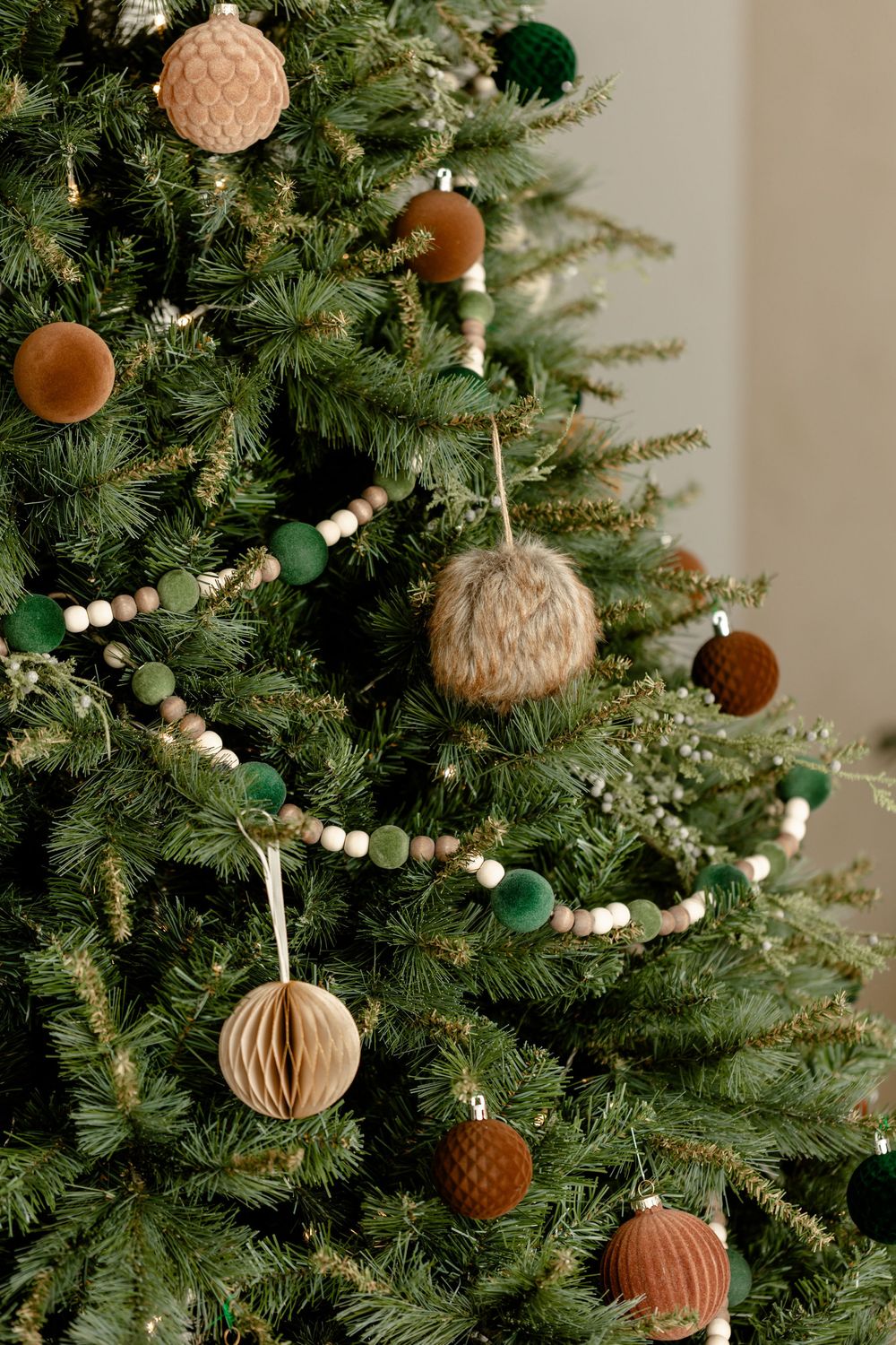 Close-up of a modern Christmas tree decorated with natural wooden beads and textured ornaments in earth tones.
