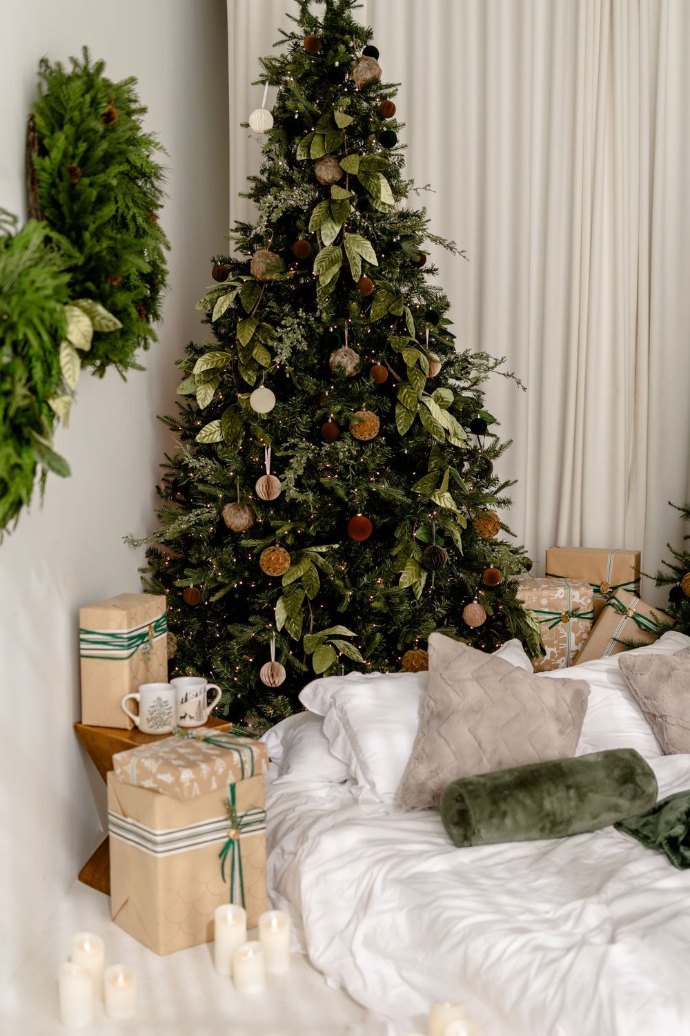 Cozy Christmas bedroom scene with white bedding and decorated tree adorned with baubles against a light backdrop.