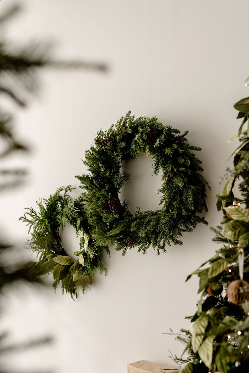 Fresh evergreen holiday wreath detail against a white wall with soft natural lighting.