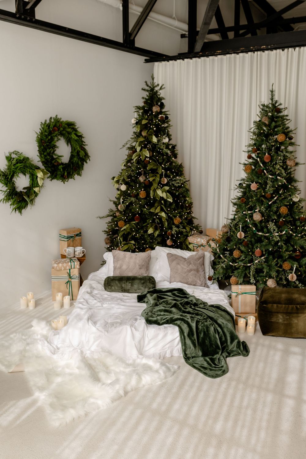 Cozy Christmas scene with decorated trees, white bedding, and wrapped presents in a minimalist white room.