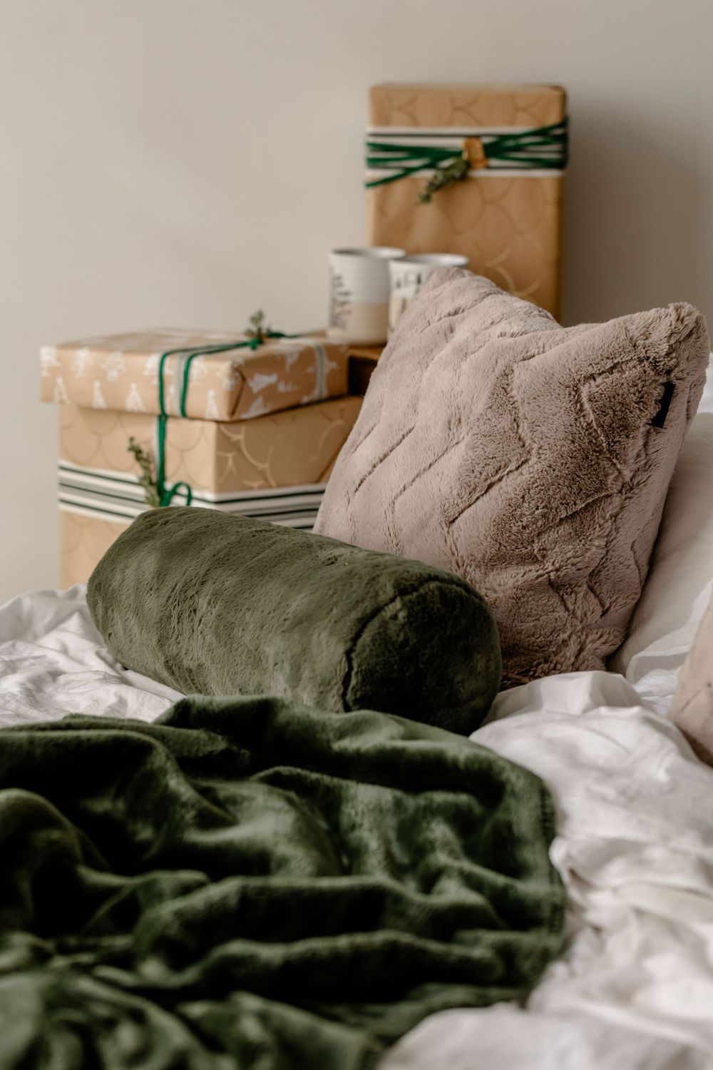 Brown and olive green throw pillows with wrapped gifts on white bedding in a festive holiday setting.