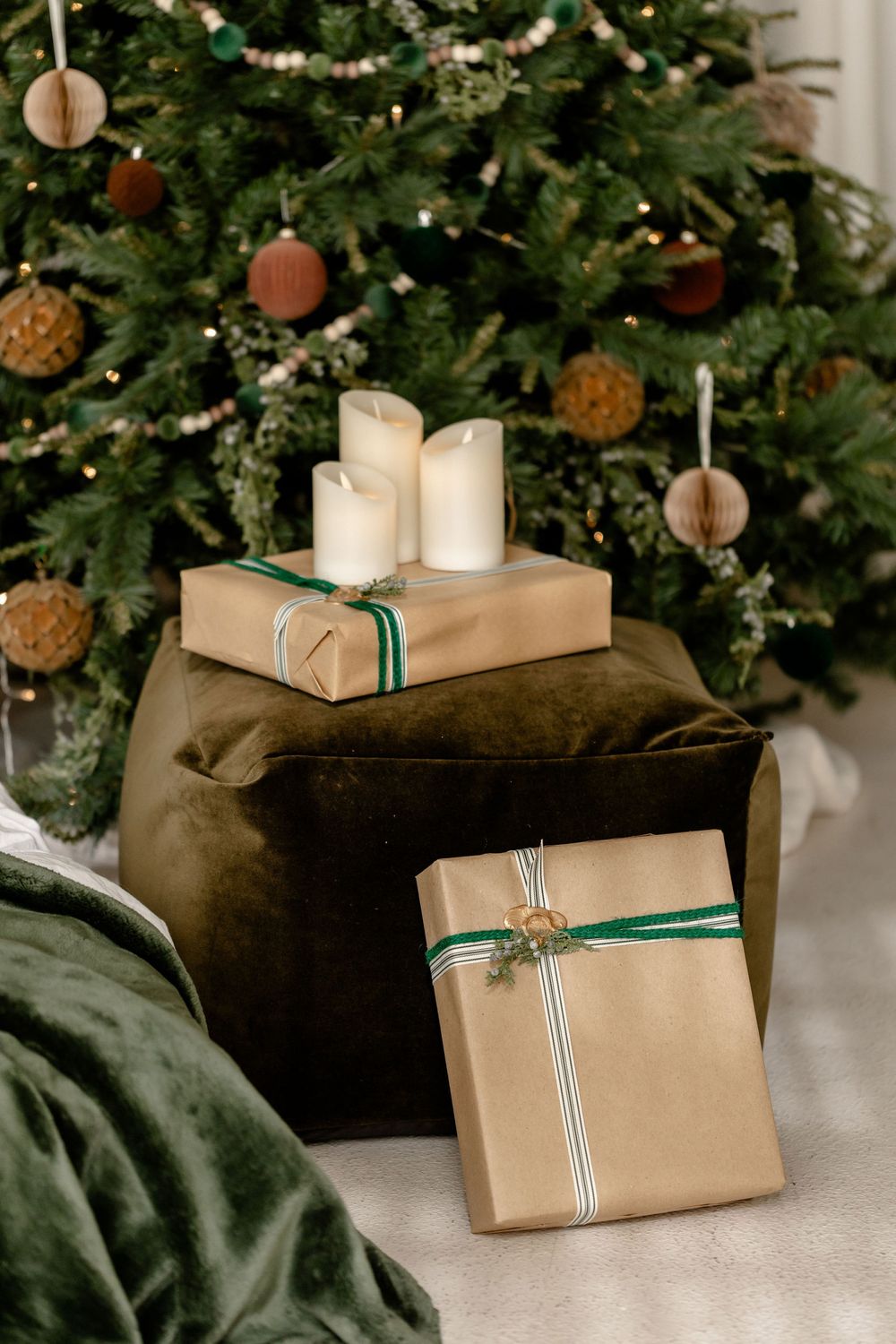 Kraft paper wrapped Christmas presents with green ribbons displayed near a decorated tree and velvet pillows.