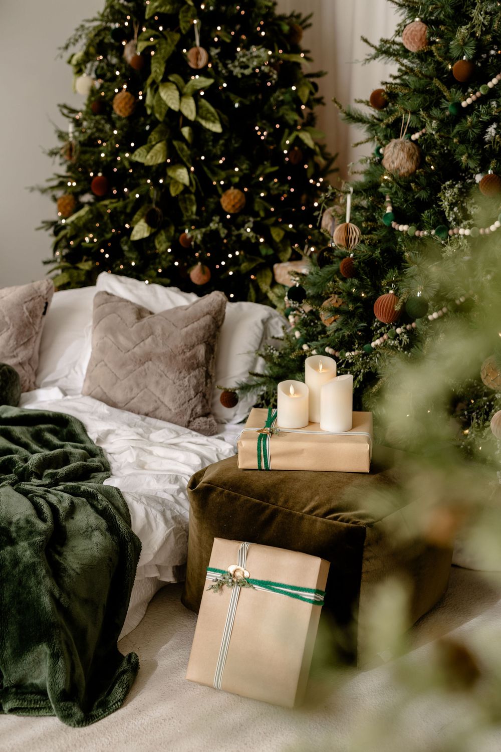 Cozy Christmas living room with decorated tree, green blanket, throw pillows, candles and wrapped present.