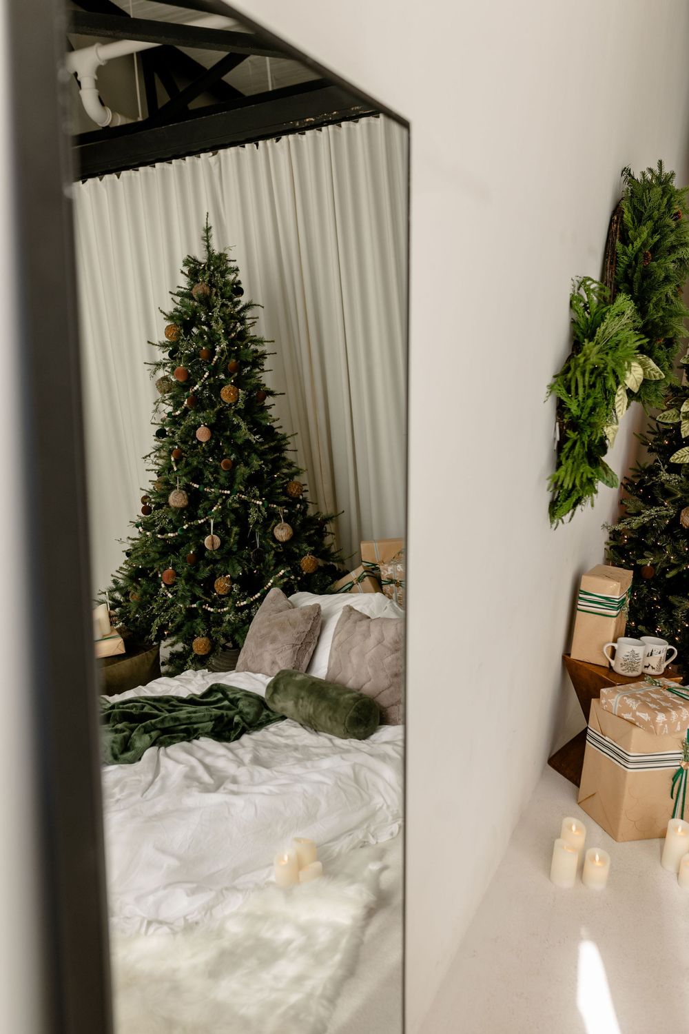 Modern minimalist bedroom with Christmas tree, white bedding, and natural holiday decorations.