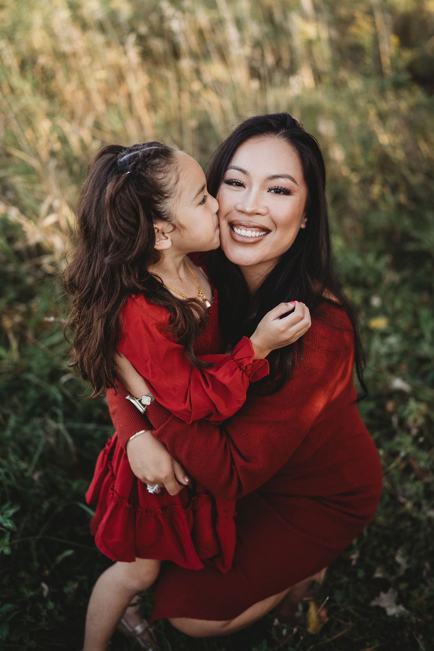 Joyful mother and daughter embracing in red outfits against a natural backdrop.