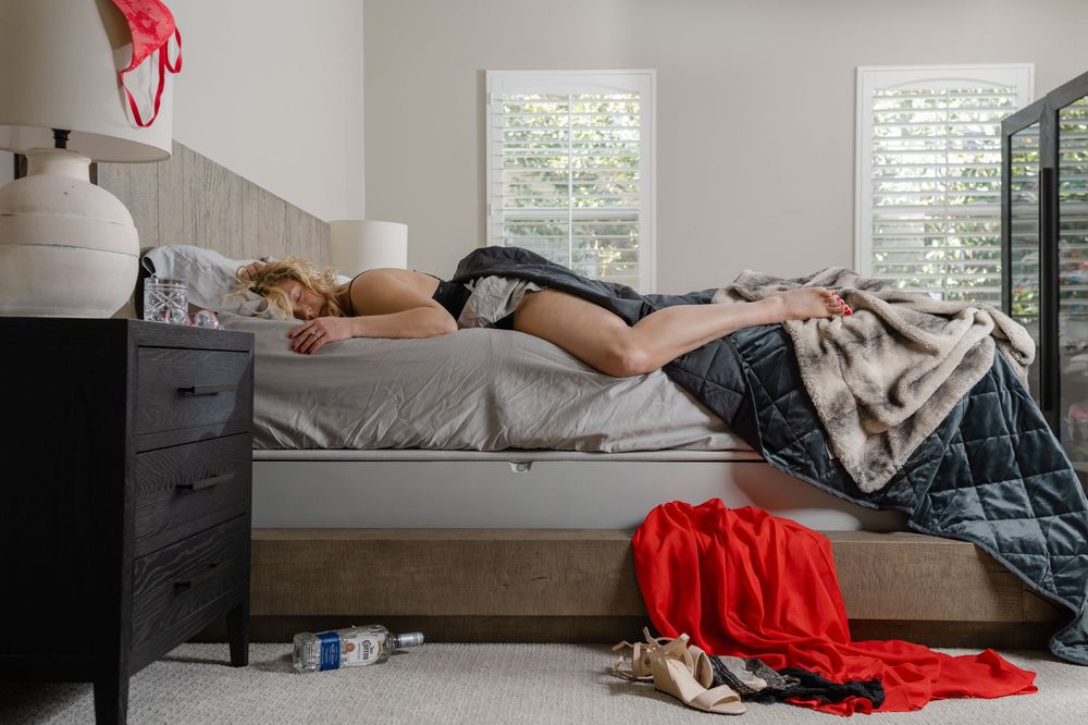 Person lying down on a bed with red blanket in a sunlit room.