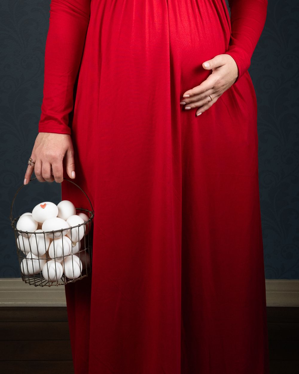 Person in a flowing red dress holding a wire basket with white eggs against a dark background.