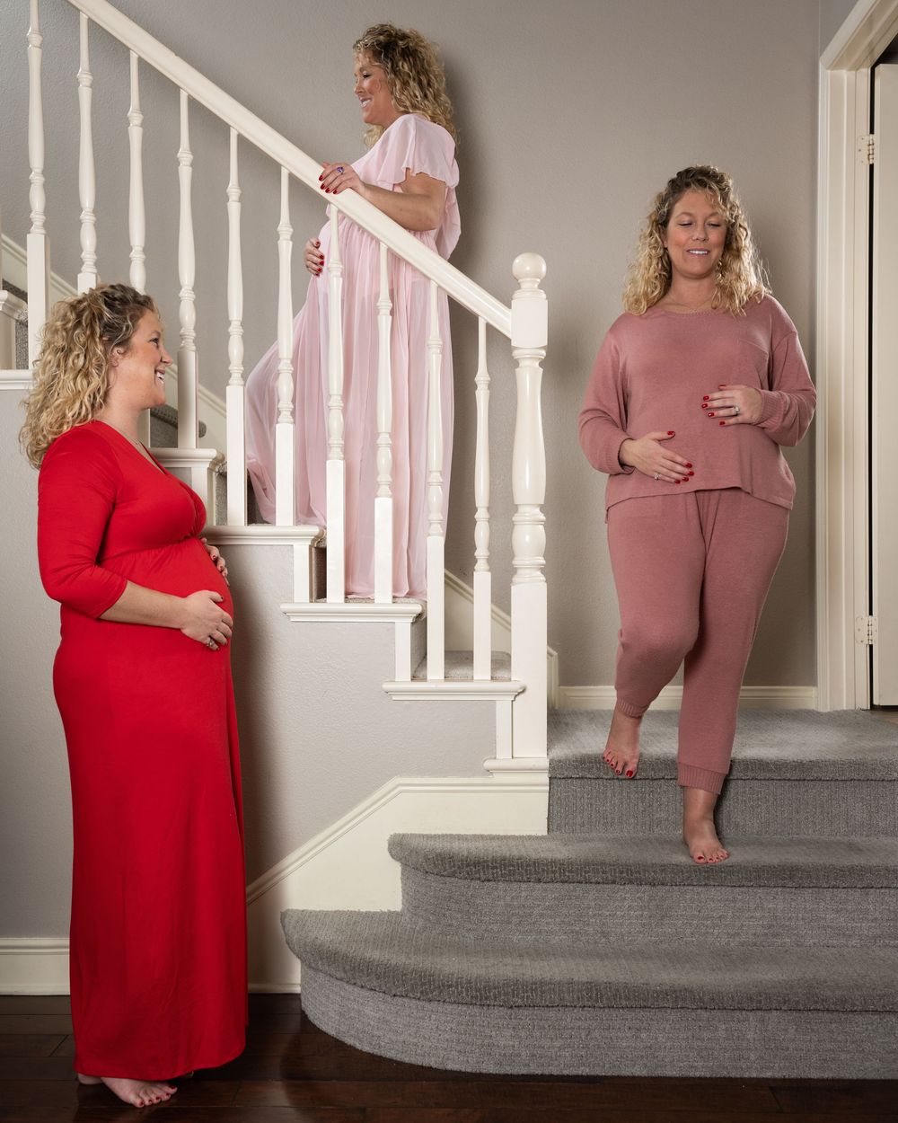 Three people in loungewear stand on gray carpeted stairs in a home interior.
