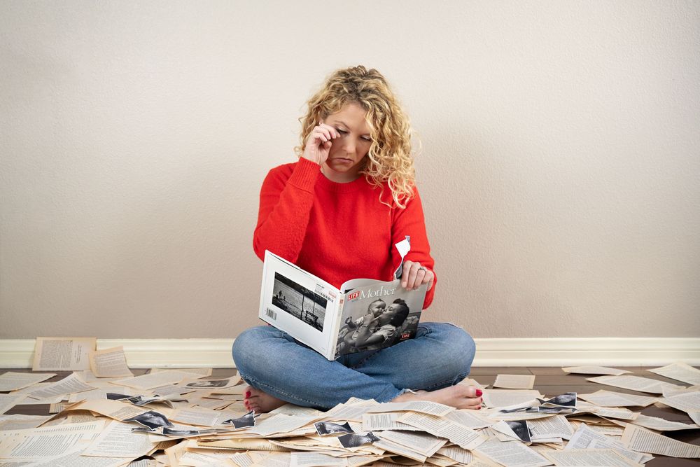 Person sitting cross-legged on floor surrounded by scattered photographs and memories.