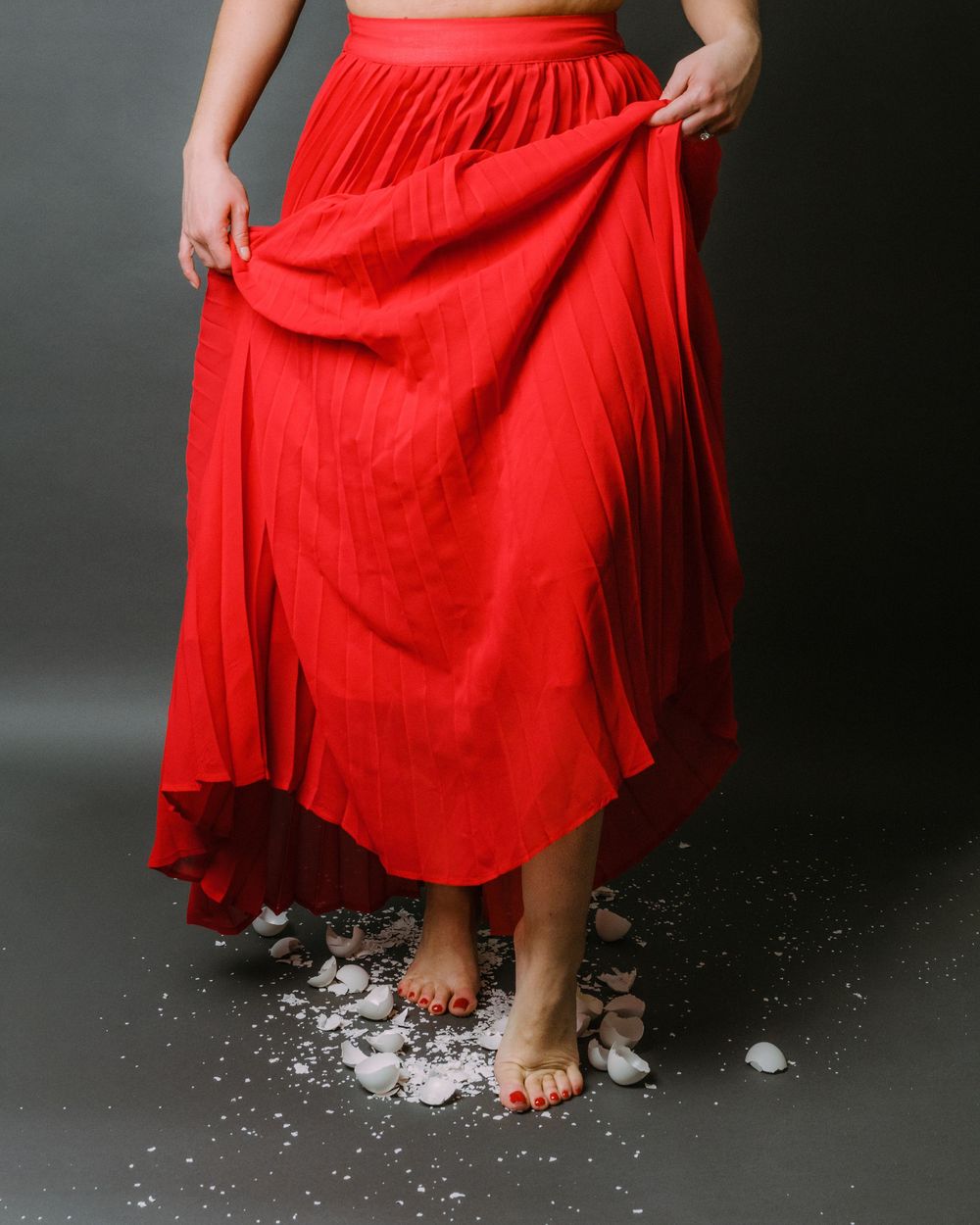 Red flowing skirt is lifted by wind creating movement over scattered confetti on dark floor.