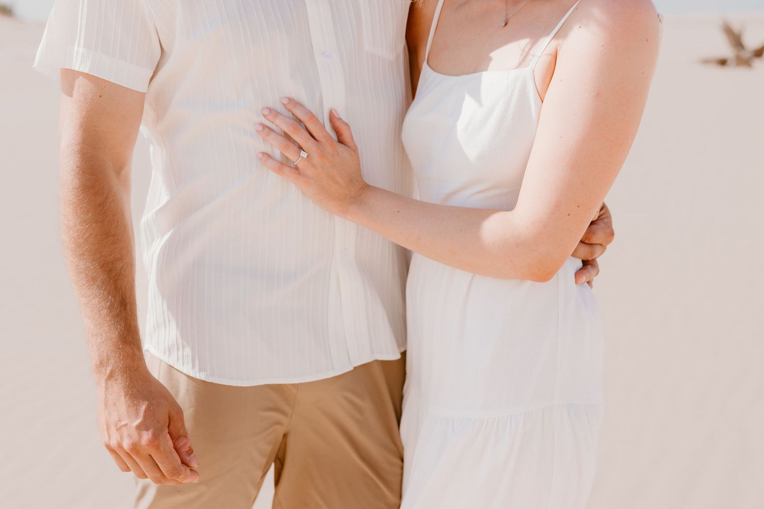 A close-up view of a couple wearing white clothing embracing in soft natural light.