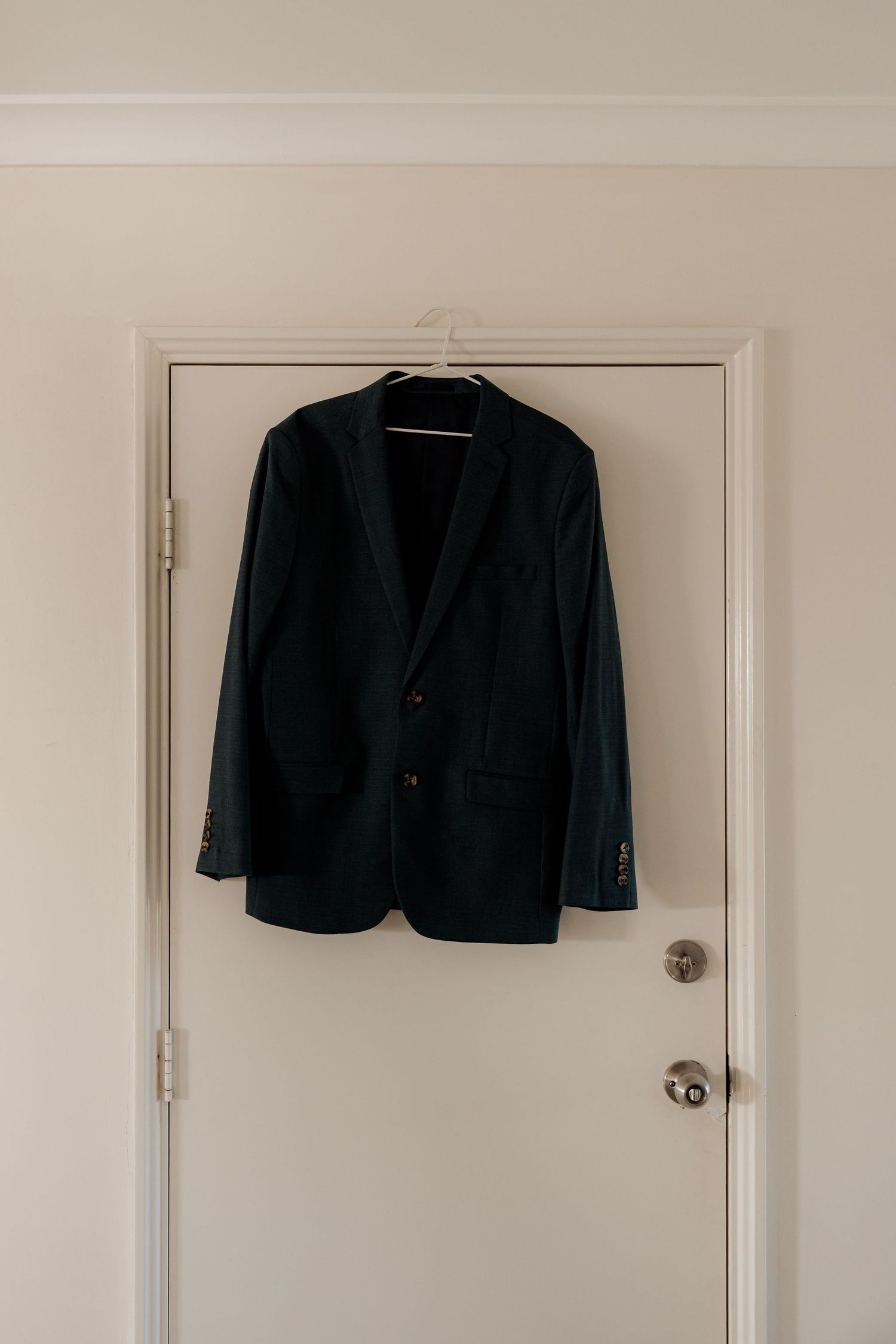 Black blazer jacket hanging on a white wall against minimal, clean interior.