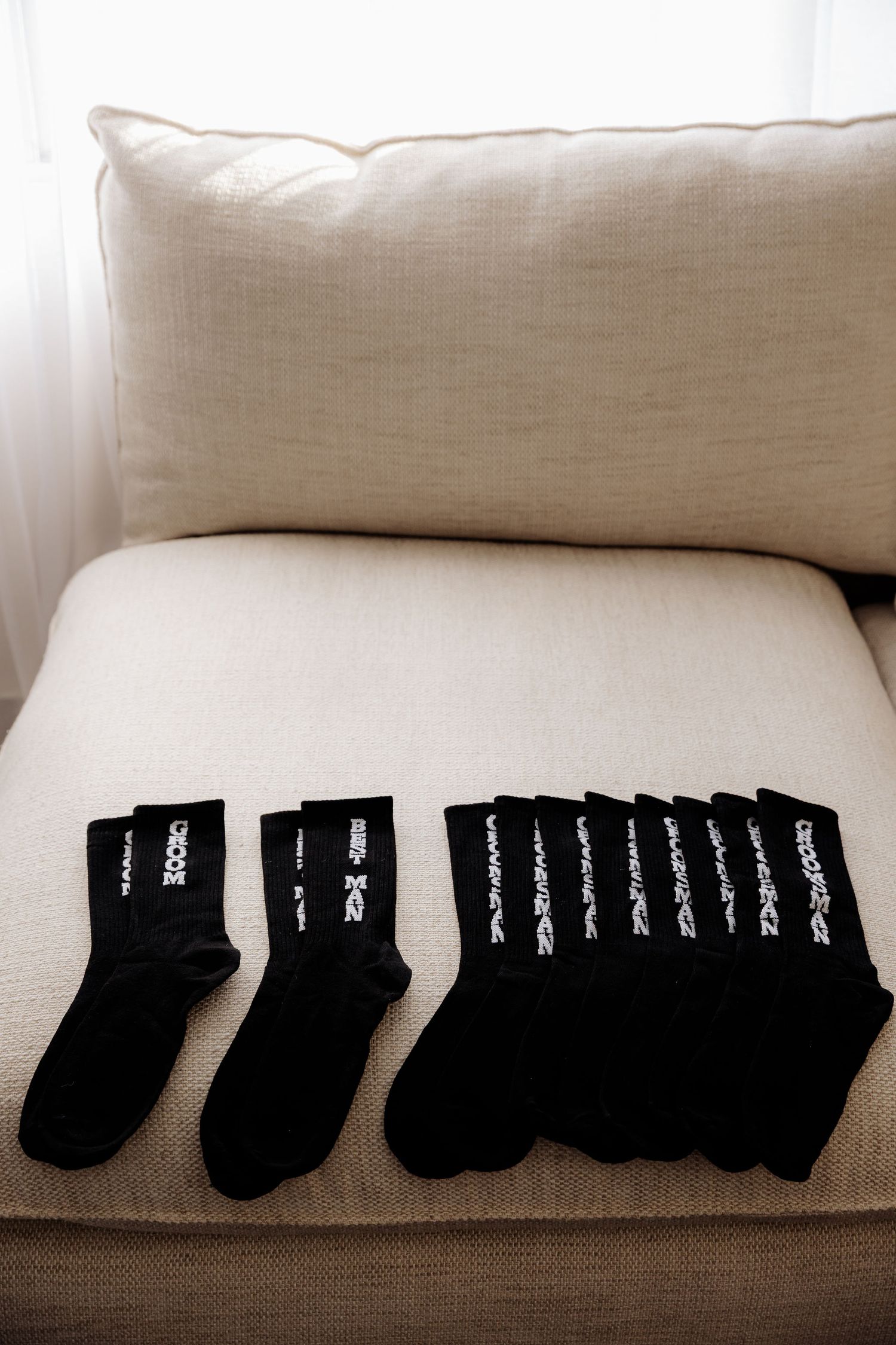 Black socks with text patterns arranged on a beige couch cushion next to a light colored pillow.