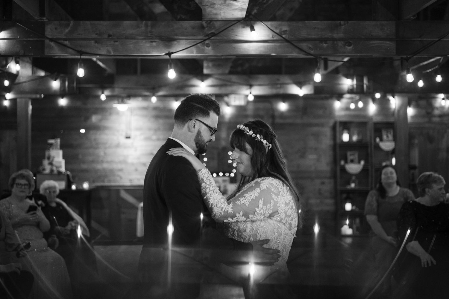 Couple shares intimate first dance under twinkling string lights in rustic barn venue during wedding reception.