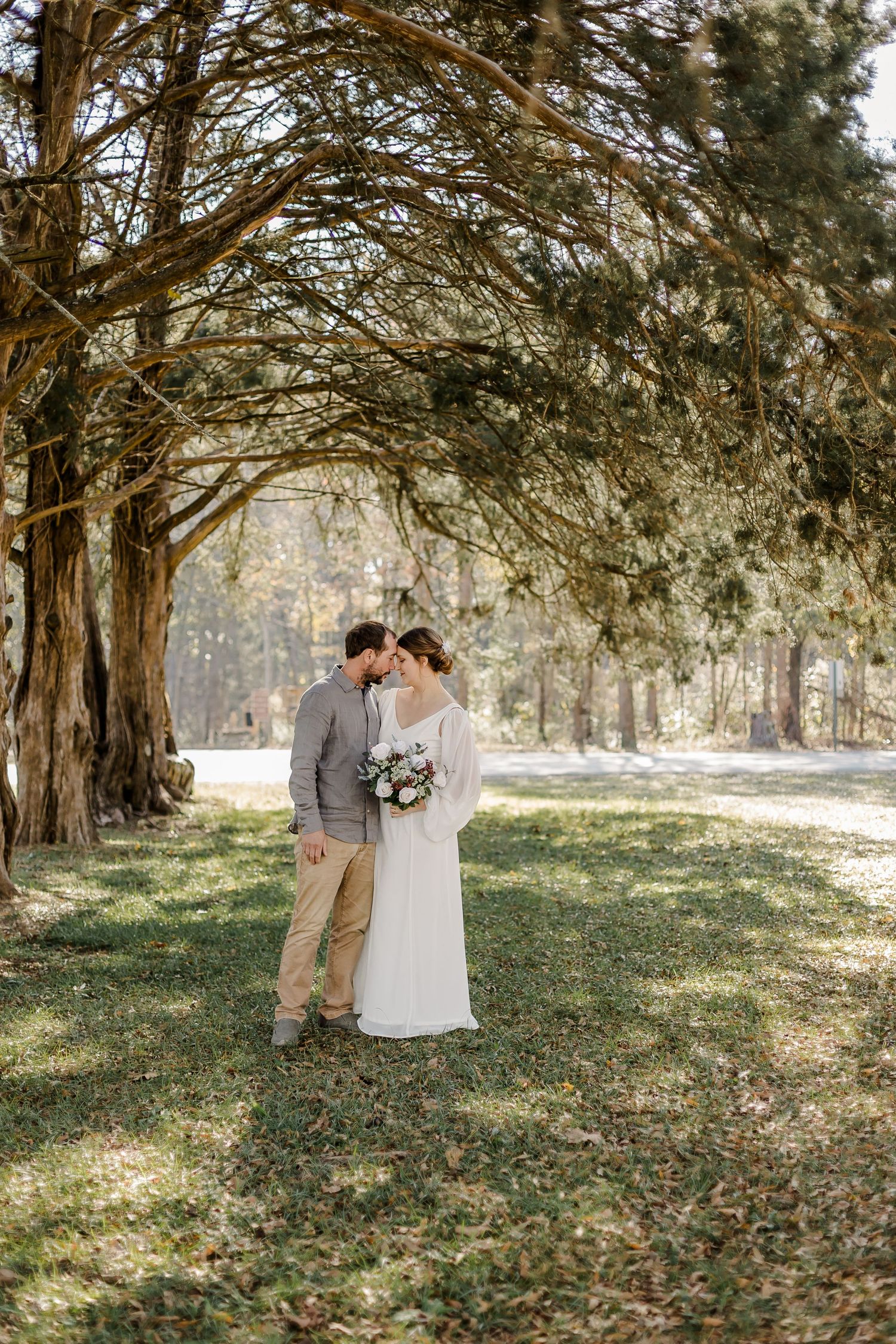 Newlyweds share tender moments under a canopy of trees in a rustic outdoor setting.