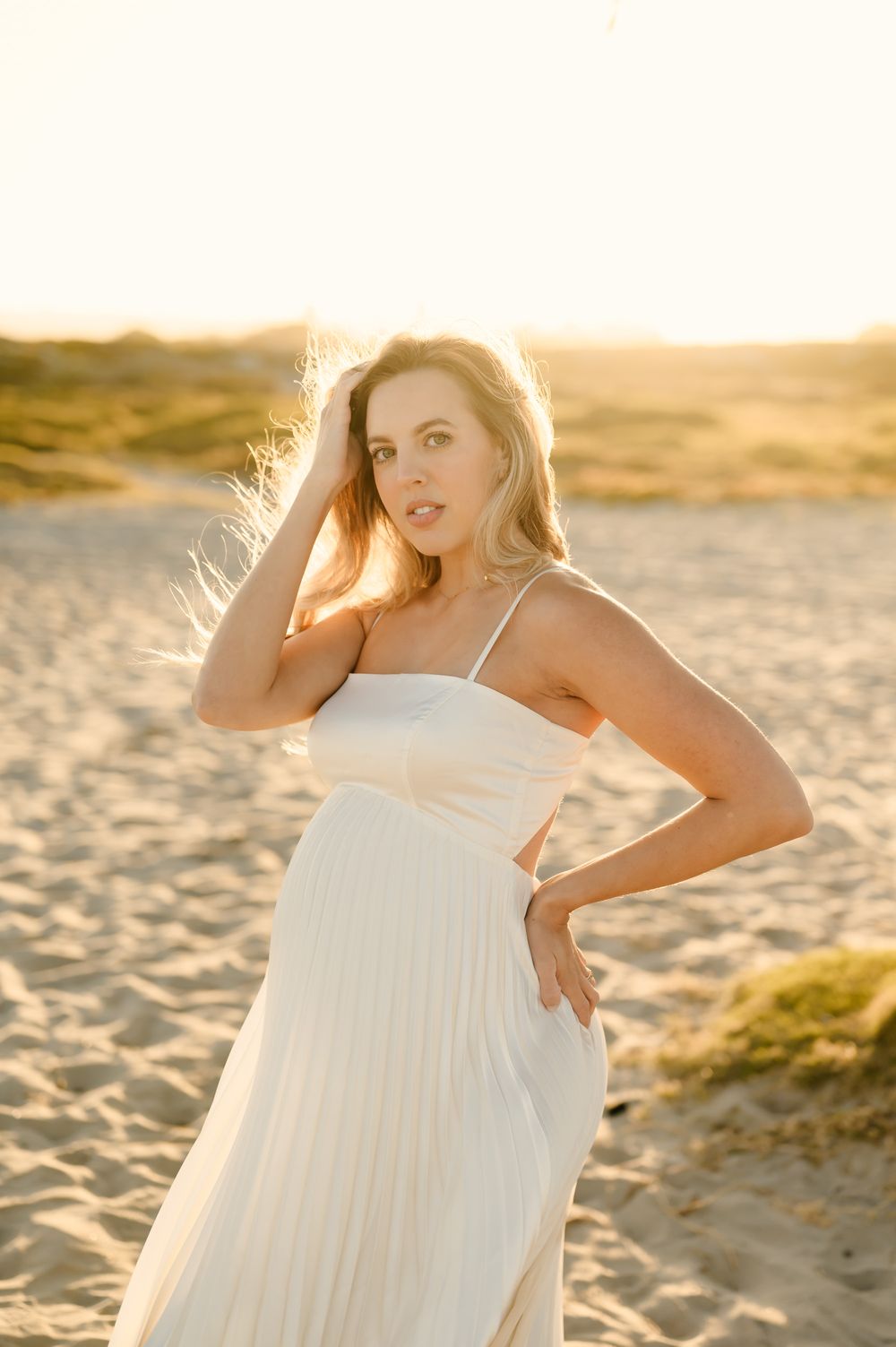 woman poses in sunshine in white dress holding her long hair during her maternity photoshoot by Ventura and Santa Barbara photographer